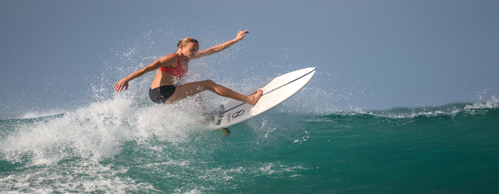 Mirissa, Sri Lanka - 04 09 2022: Athletic female surfer completes the aerial maneuver on the clear big wave. Keeping the body balance all the way. High-skilled professional surfer woman in action.